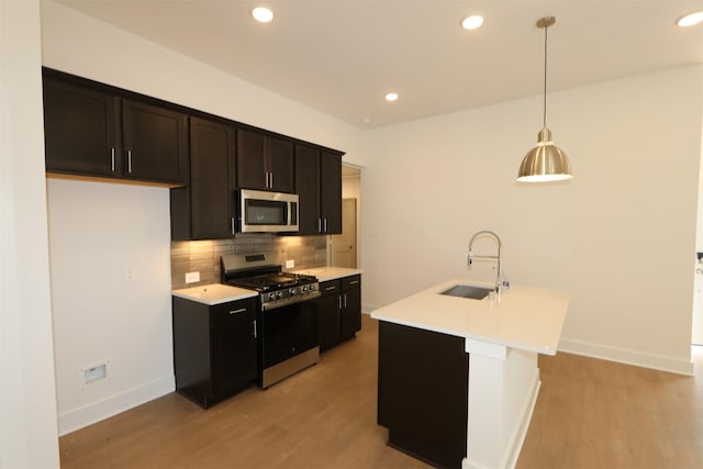 kitchen featuring a sink, light wood-style floors, light countertops, appliances with stainless steel finishes, and decorative backsplash