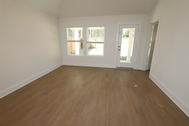 empty room featuring lofted ceiling, dark wood-type flooring, and baseboards