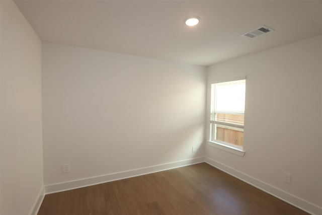 unfurnished room featuring dark wood-type flooring, visible vents, and baseboards