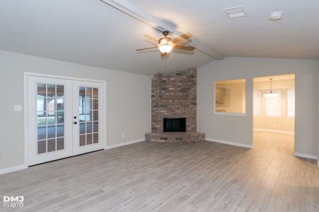 unfurnished living room with a fireplace, vaulted ceiling with beams, french doors, a wealth of natural light, and ceiling fan with notable chandelier