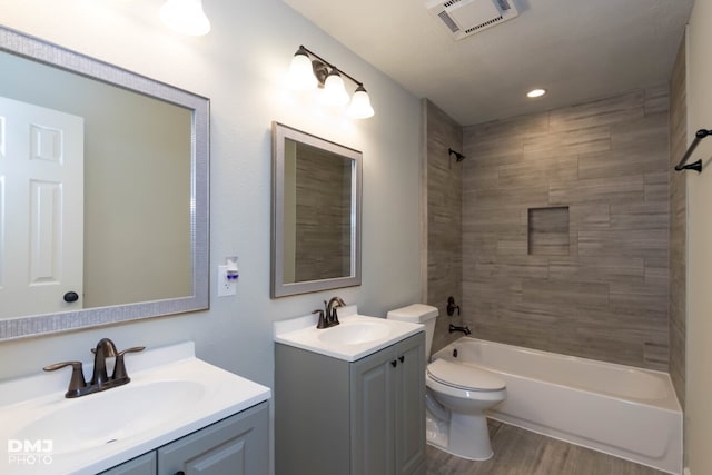 full bathroom featuring wood-type flooring, toilet, vanity, and tiled shower / bath combo