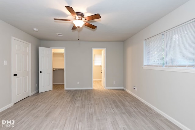 unfurnished bedroom with ceiling fan, a spacious closet, a closet, and light wood-type flooring