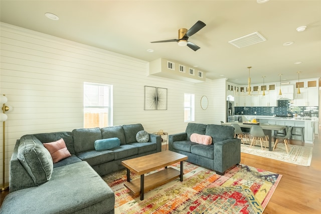 living room featuring light hardwood / wood-style flooring, a wealth of natural light, wooden walls, and ceiling fan