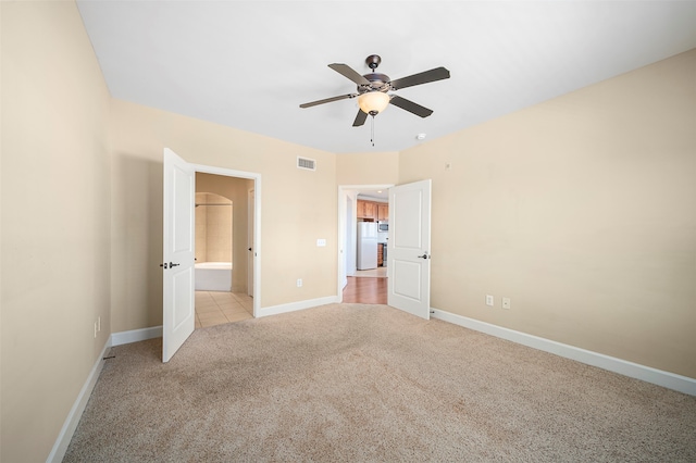 unfurnished bedroom featuring white fridge, ceiling fan, light colored carpet, and ensuite bathroom