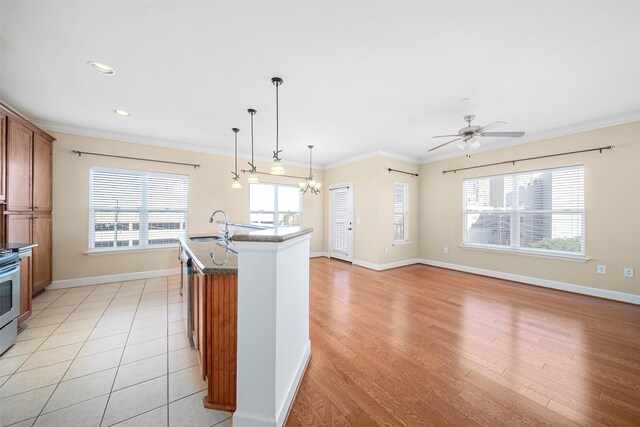 kitchen with ornamental molding, a kitchen island with sink, decorative light fixtures, light tile flooring, and ceiling fan