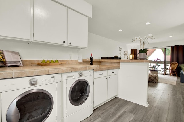 clothes washing area featuring cabinets, light hardwood / wood-style flooring, and washer and clothes dryer