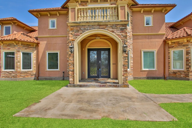 view of exterior entry with a balcony, french doors, and a yard