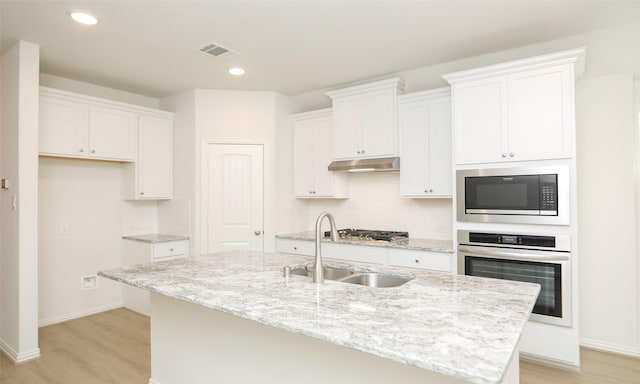 kitchen with white cabinetry, oven, built in microwave, and an island with sink