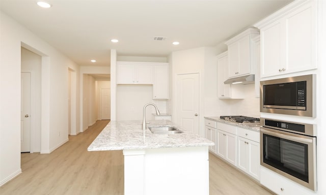 kitchen with white cabinetry, sink, light stone counters, a center island with sink, and appliances with stainless steel finishes