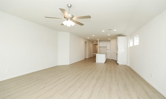 unfurnished living room featuring ceiling fan, light wood-type flooring, and sink