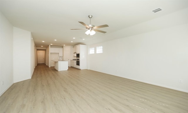 unfurnished living room with light wood-type flooring, ceiling fan, and sink