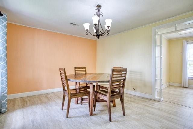 dining space with light wood finished floors, baseboards, visible vents, ornamental molding, and an inviting chandelier