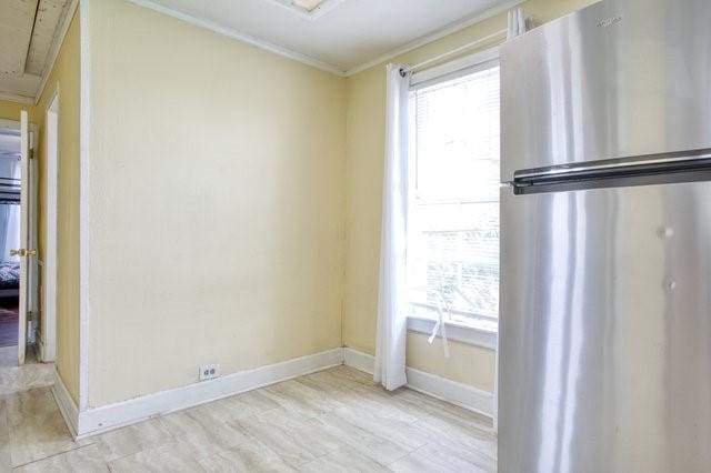 empty room with light wood finished floors, attic access, ornamental molding, and baseboards