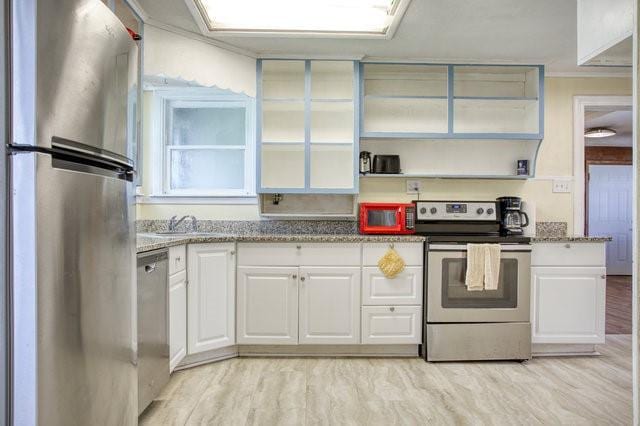 kitchen featuring appliances with stainless steel finishes, white cabinetry, light wood-style floors, and light stone countertops