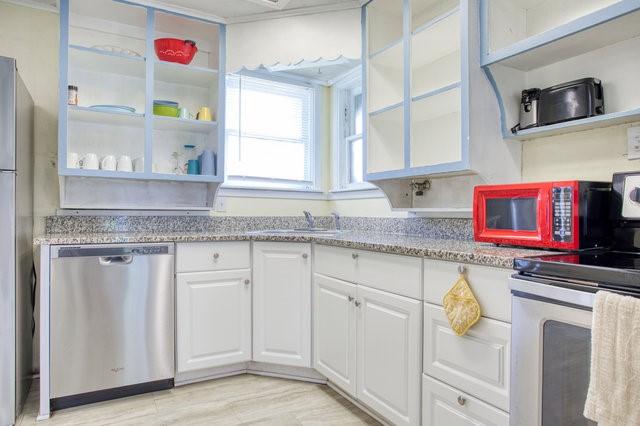 kitchen with light stone counters, open shelves, appliances with stainless steel finishes, white cabinetry, and a sink