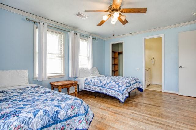 bedroom with wood finished floors, a ceiling fan, baseboards, visible vents, and crown molding