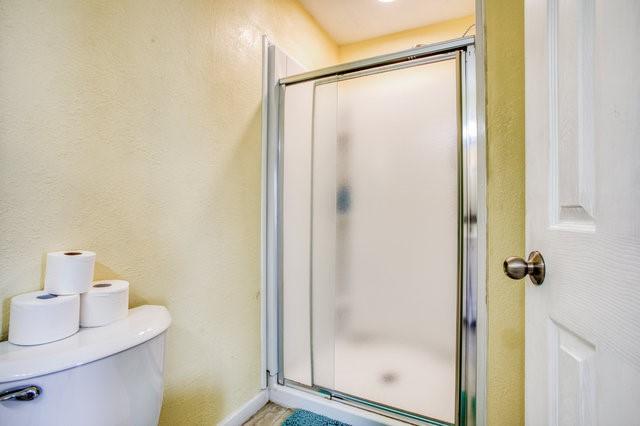 full bathroom with a textured wall, a shower stall, and toilet