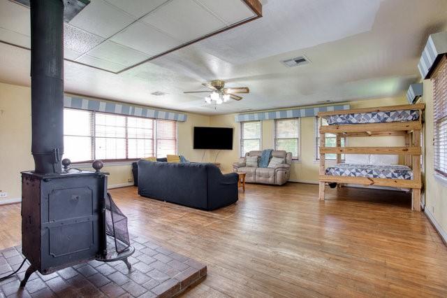 living area with baseboards, visible vents, ceiling fan, wood finished floors, and a wood stove