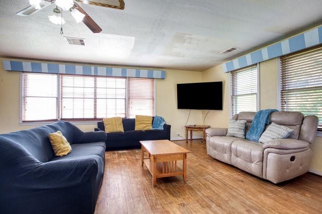 living room with a ceiling fan, visible vents, a textured ceiling, and wood finished floors