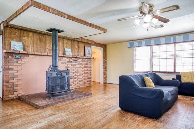 living room featuring wood finished floors, a wood stove, and a ceiling fan