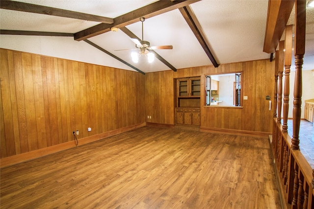 unfurnished living room featuring vaulted ceiling with beams, hardwood / wood-style flooring, ceiling fan, and wooden walls