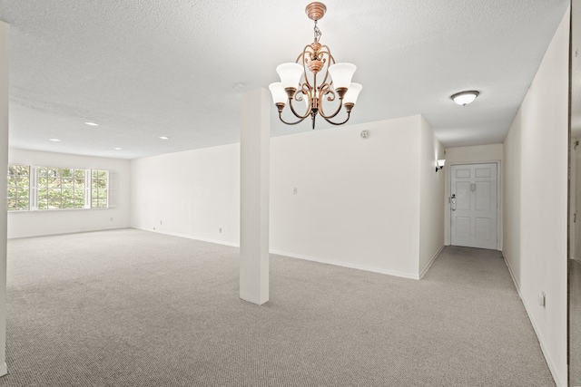 carpeted spare room with a notable chandelier and a textured ceiling