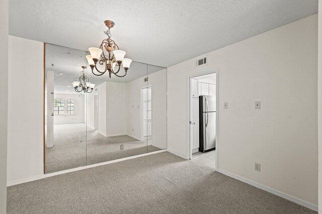 unfurnished dining area with a textured ceiling, a notable chandelier, and light colored carpet