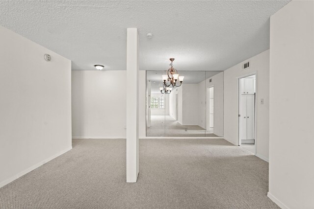 carpeted empty room featuring a notable chandelier and a textured ceiling