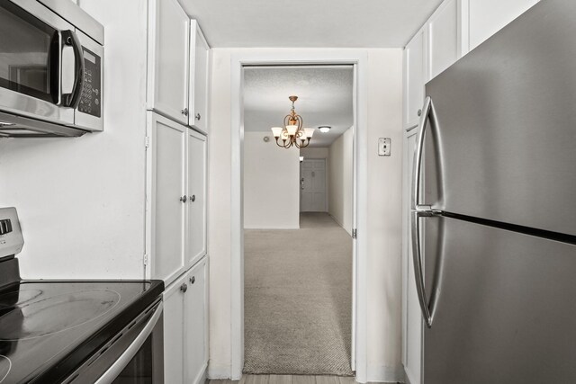 kitchen with white cabinetry, appliances with stainless steel finishes, an inviting chandelier, and light carpet