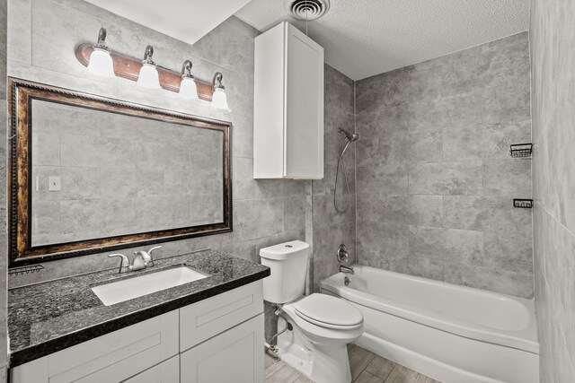 full bathroom with vanity, a textured ceiling, tile walls, toilet, and tiled shower / bath combo