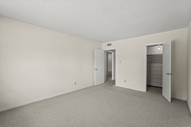 unfurnished bedroom featuring a closet, a spacious closet, a textured ceiling, and light carpet