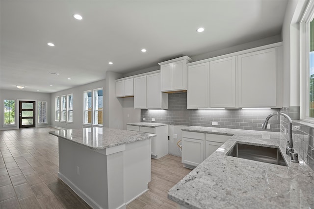 kitchen with tasteful backsplash, white cabinets, a kitchen island, light stone countertops, and sink