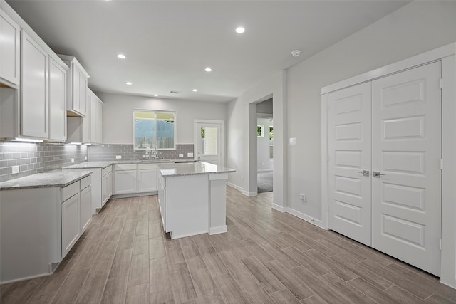 kitchen featuring white cabinets, light stone counters, backsplash, light hardwood / wood-style floors, and a center island