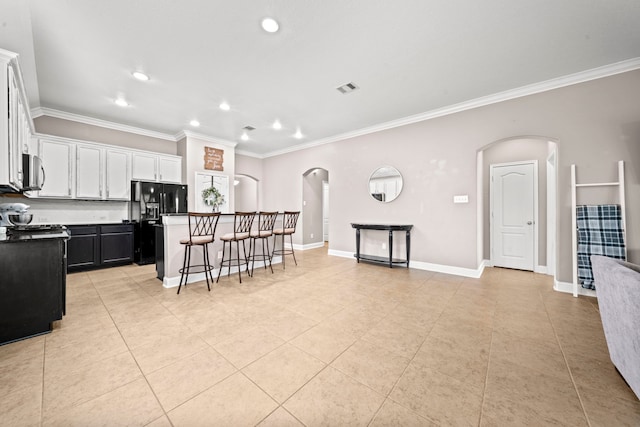 kitchen with ornamental molding, black fridge, a breakfast bar, a kitchen island, and white cabinets