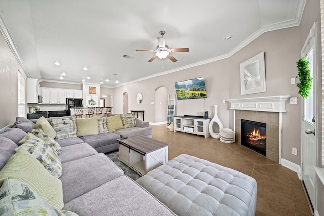 living room featuring a tiled fireplace, ceiling fan, tile patterned flooring, and crown molding