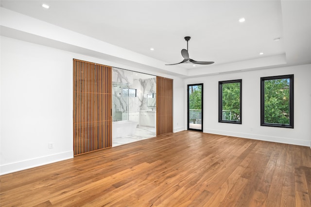 interior space featuring ceiling fan, connected bathroom, light wood-type flooring, and a tray ceiling