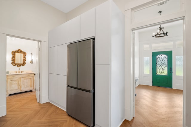 kitchen with sink, a chandelier, white cabinets, light parquet flooring, and stainless steel refrigerator