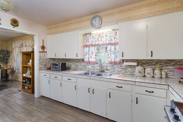 kitchen featuring backsplash, sink, white cabinetry, and stove