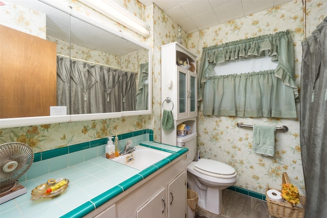 full bath with toilet, wood finished floors, vanity, a shower with curtain, and wallpapered walls