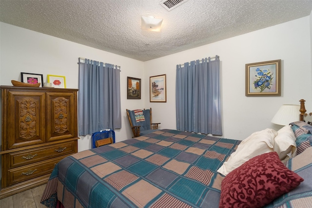 bedroom with visible vents, a textured ceiling, and wood finished floors