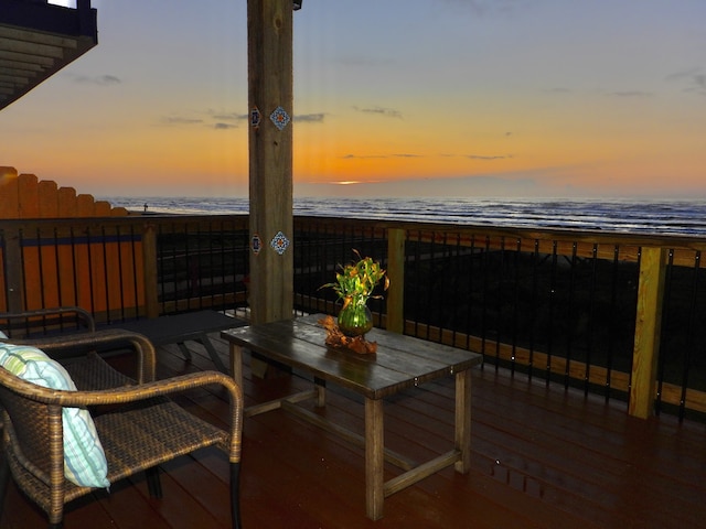 deck at dusk featuring a view of the beach and a water view