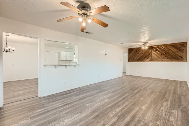 unfurnished living room with ceiling fan with notable chandelier, a textured ceiling, and light wood-type flooring