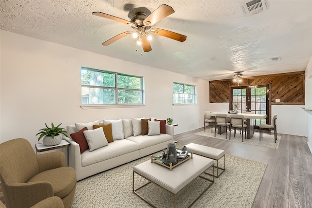 living room with french doors, wooden walls, hardwood / wood-style flooring, ceiling fan, and a textured ceiling