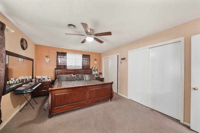 bedroom with multiple closets, visible vents, a ceiling fan, light carpet, and baseboards