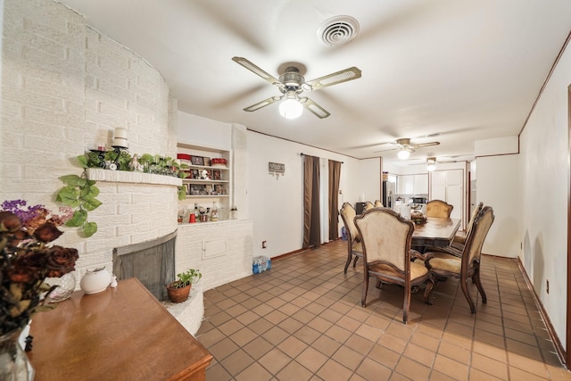 dining room featuring visible vents, a brick fireplace, ceiling fan, baseboards, and tile patterned floors