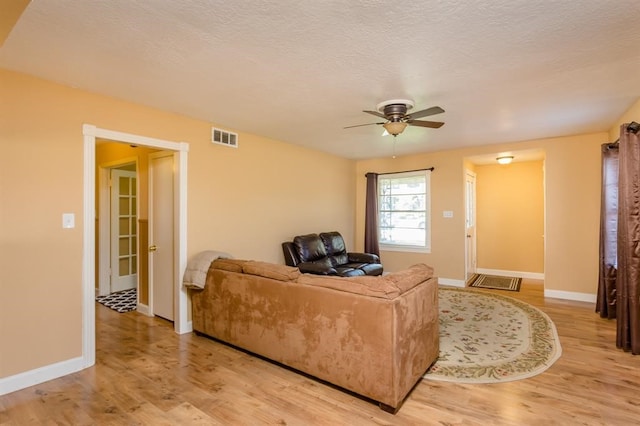 living room with ceiling fan, light hardwood / wood-style floors, and a textured ceiling