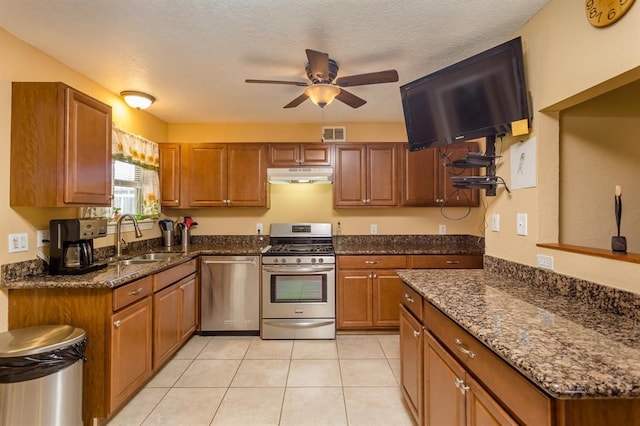 kitchen with dark stone counters, ceiling fan, light tile flooring, sink, and appliances with stainless steel finishes