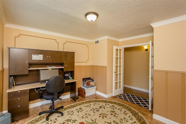 office area featuring built in desk, light hardwood / wood-style floors, a textured ceiling, and crown molding