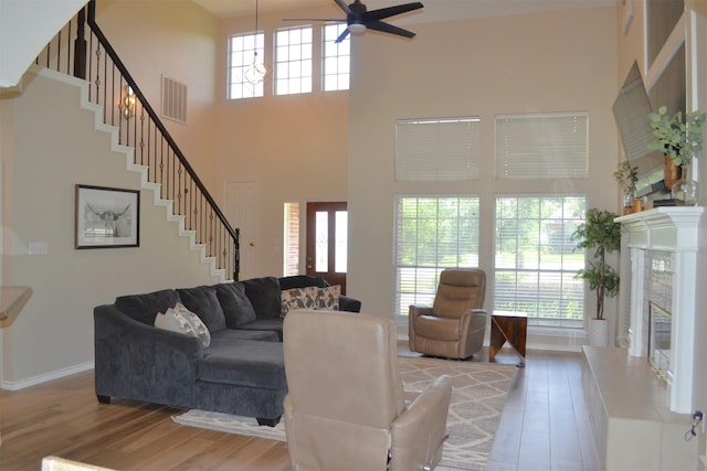 living room featuring hardwood / wood-style floors, ceiling fan, a high ceiling, and a tiled fireplace