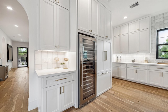 kitchen with light hardwood / wood-style floors, white cabinetry, beverage cooler, and tasteful backsplash